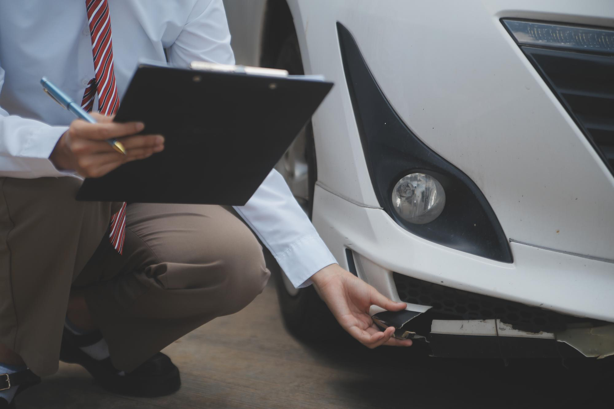 Kfz-Sachverständiger dokumentiert den Schaden am Stoßfänger eines weißen Autos